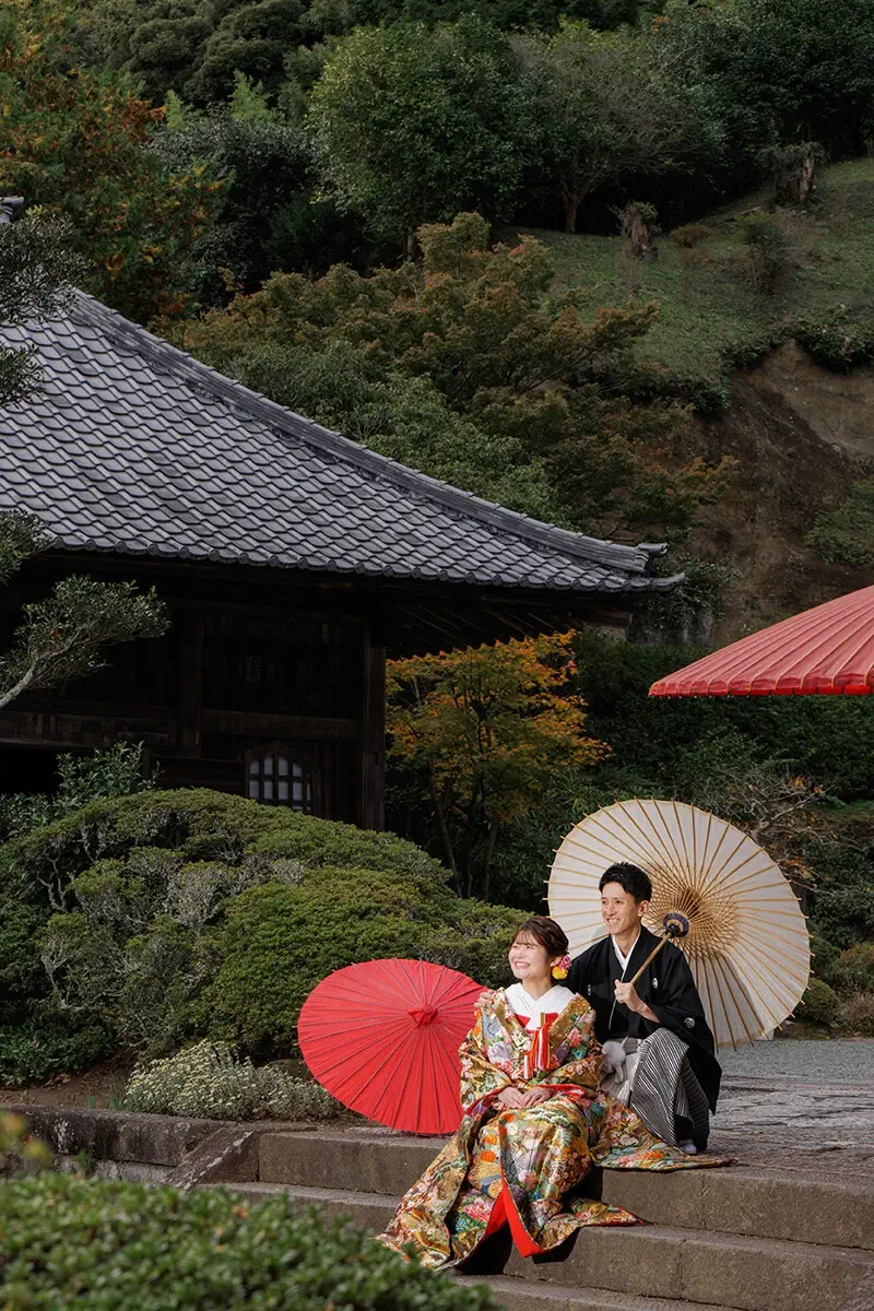 鎌倉の緑深い山奥で、色打掛の新郎新婦が印象的な階段を背景に和装前撮りを行うウェディングフォト