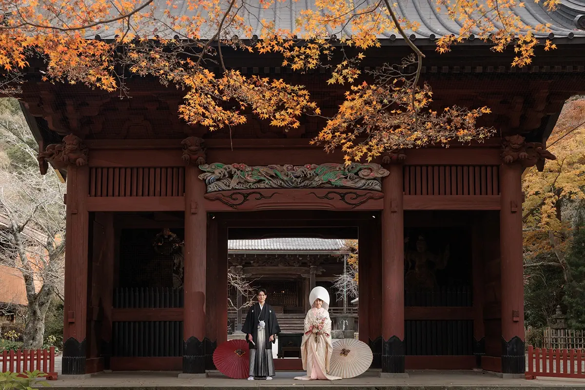 鎌倉・妙本寺の二天門前で白無垢姿の新婦と和装の新郎が紅葉に囲まれて佇むフォトウェディング・前撮り写真