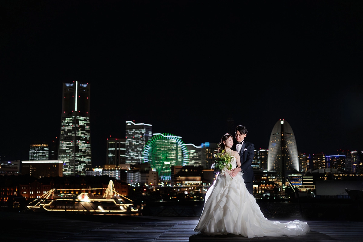 横浜・大桟橋でウェディングドレス姿とタキシード姿の新婦と新郎がみなとみらいの夜景を背景に撮影するフォトウェディング・前撮り写真