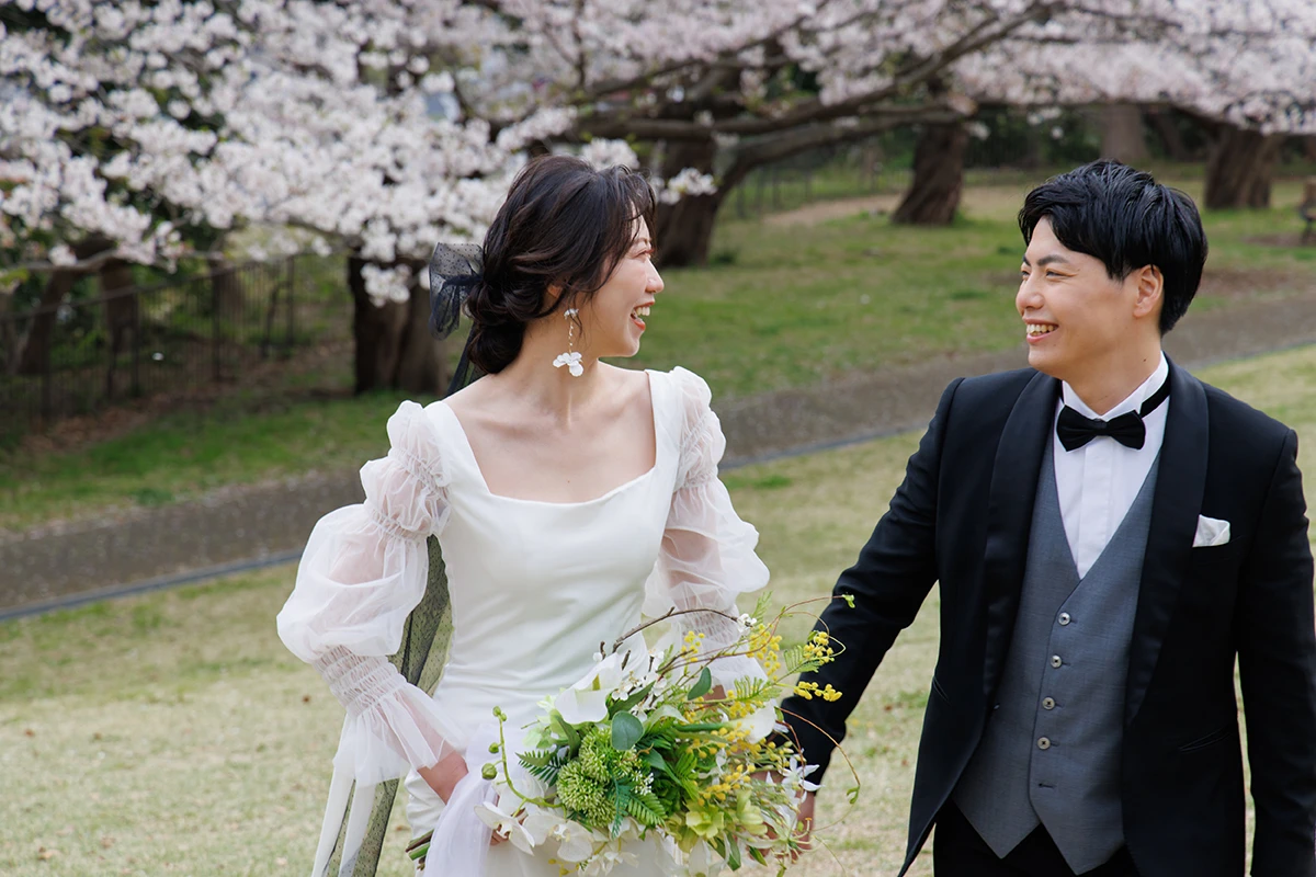 スクエアネックのウェディングドレスを着た新婦とタキシード姿の新郎が向かい合ってほほ笑むウェディングフォト
