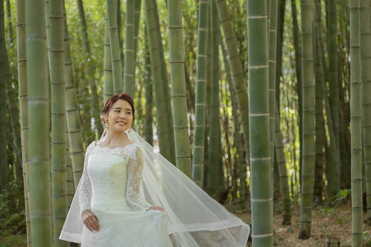 総レースをあしらったウェディングドレスを着用する新婦が竹林の中でほほ笑むウェディングフォト