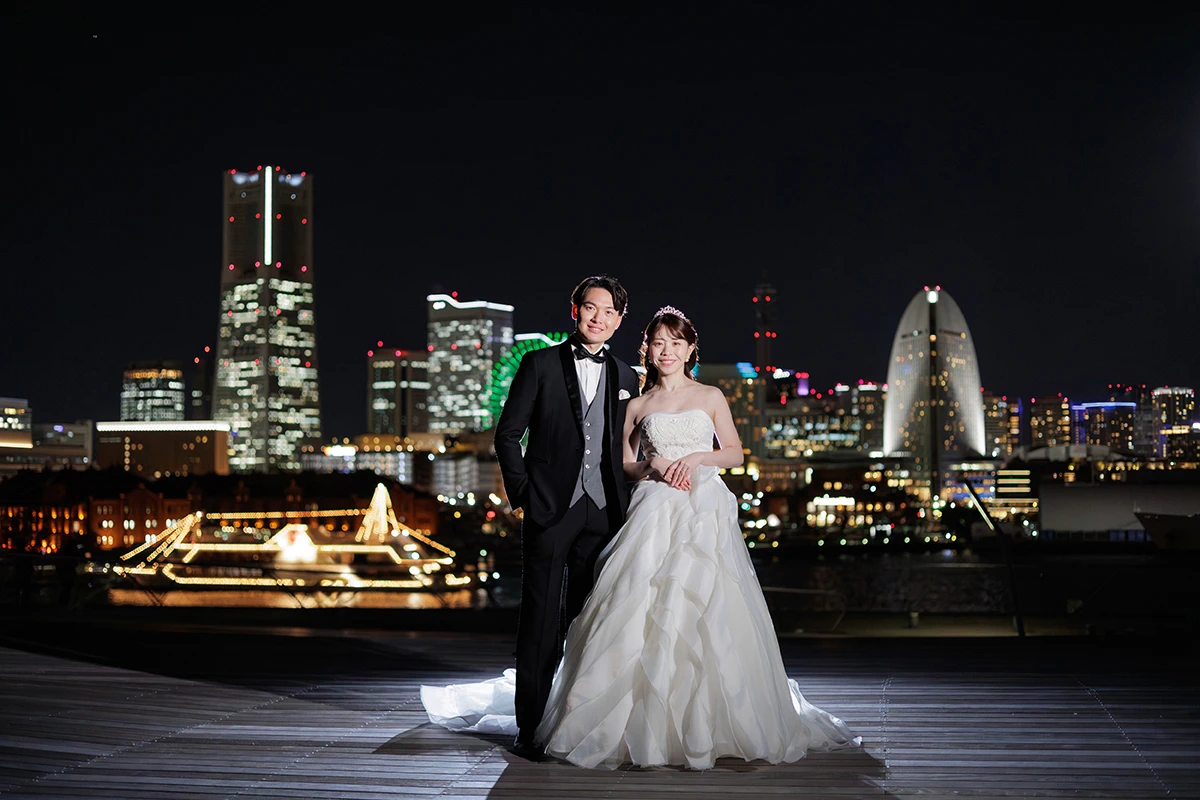 夜景の大桟橋でプリンセスラインのウェディングドレスを着用した新郎新婦がほほ笑むウェディングフォト