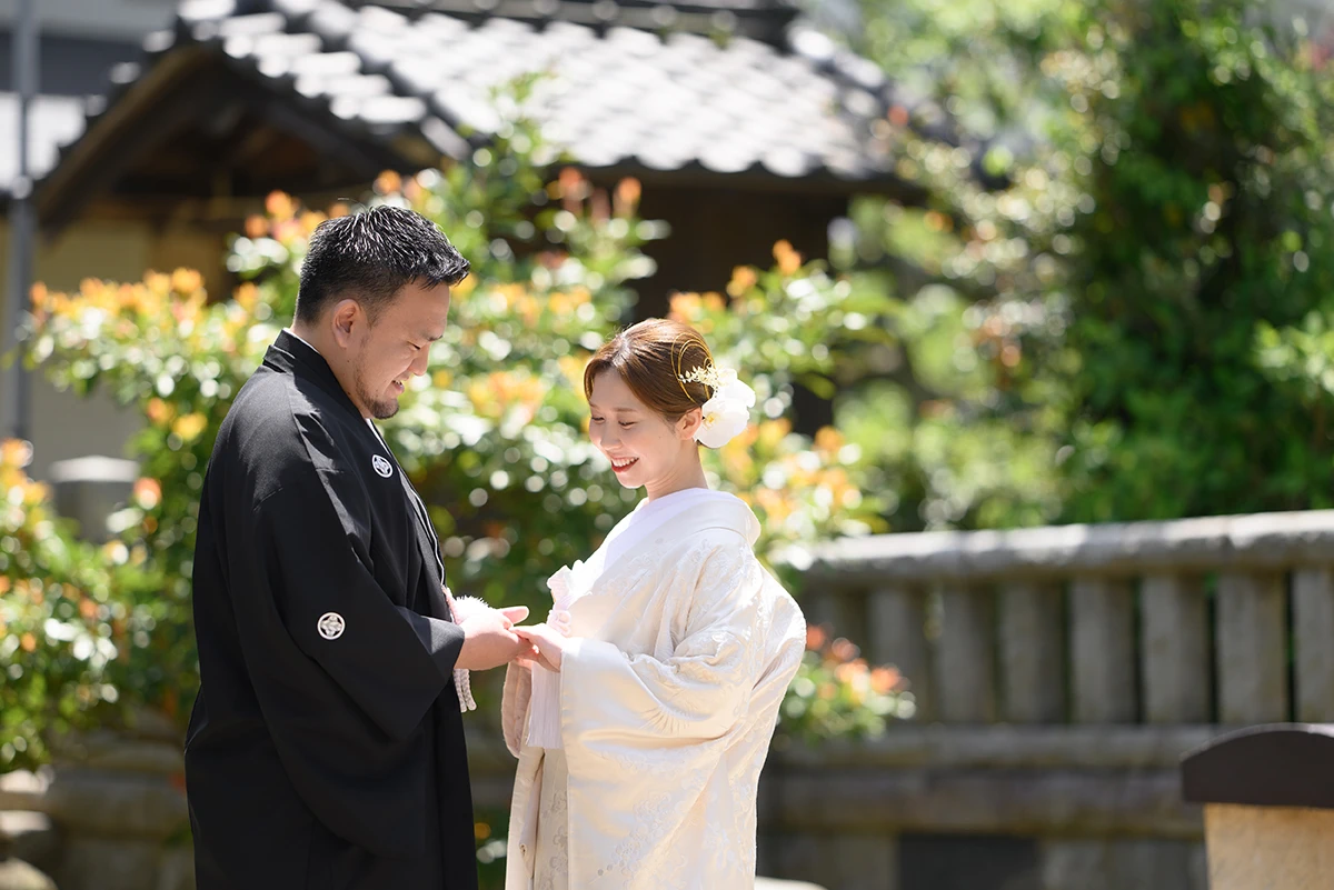 鎌倉本店の隣の神社で白無垢を着た新婦と紋付袴を着た新郎が手を取り合ってほほ笑む和装前撮りフォト