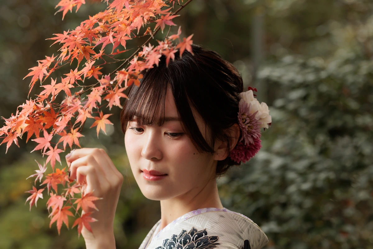 色づいた紅葉の枝に手を添え、白地に黒の柄が入った振袖姿の女性の表情を捉えた鎌倉の成人式前撮り。