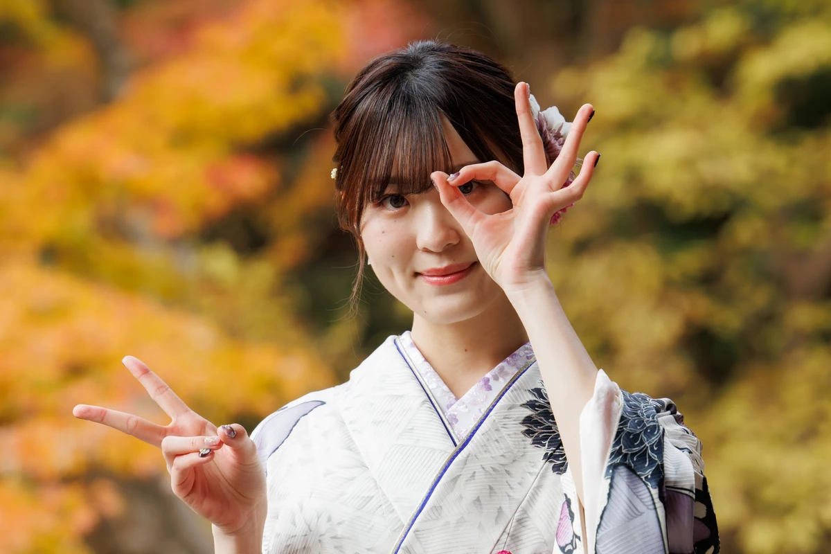 秋色の紅葉を背景に、白地に黒の柄が入った振袖姿の女性が両手で「20」を表現するポーズを見せる鎌倉の成人式前撮り。