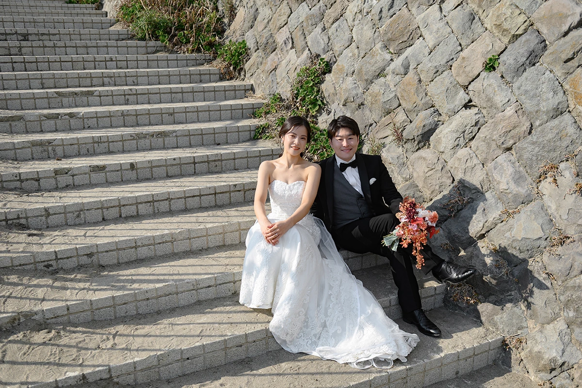 由比ガ浜でウェディングドレスとタキシードを着用した新郎新婦が階段に座って写る洋装前撮り