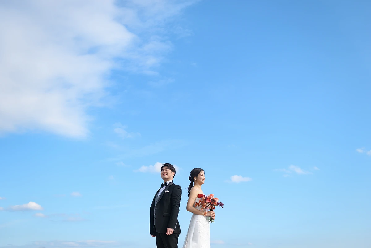 由比ガ浜でウェディングドレスとタキシードを着用した新郎新婦が青空を背景に写る洋装前撮り