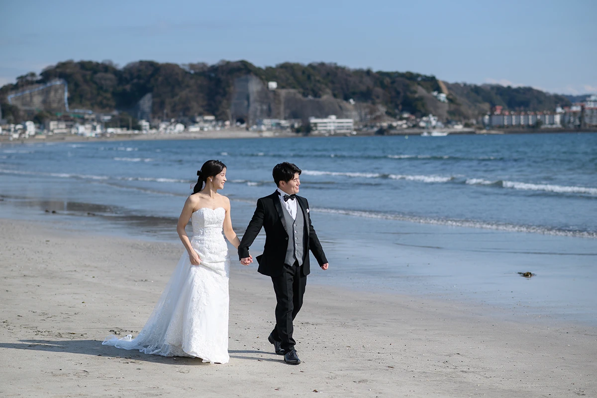 由比ガ浜でウェディングドレスとタキシードを着用した新郎新婦が海岸線を歩く洋装前撮り