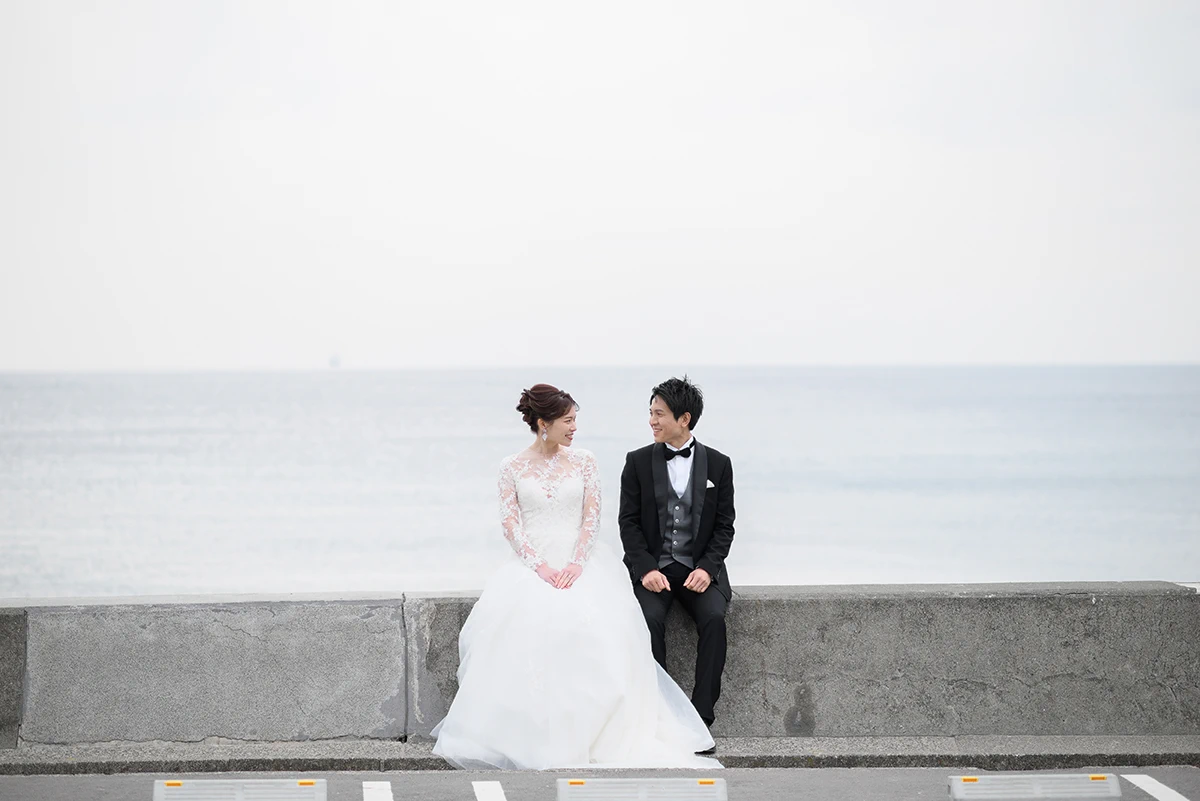 七里ガ浜でウェディングドレスとタキシードを着用した新郎新婦が座って写る洋装前撮り