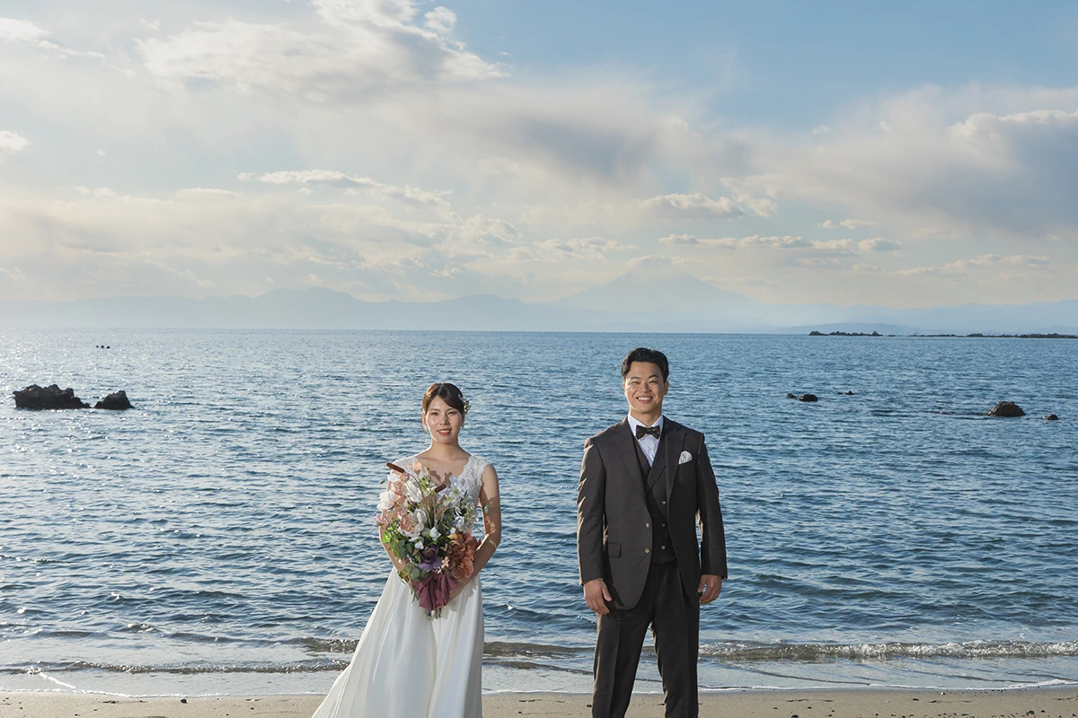 一色海岸でウェディングドレスとタキシードを着用した新郎新婦が海と富士山を背景に写る洋装前撮り