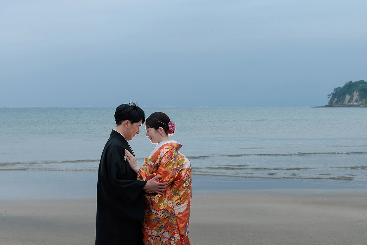 由比ガ浜で色打掛と紋付袴を着用した新郎新婦が向かい合ってほほ笑む和装前撮り