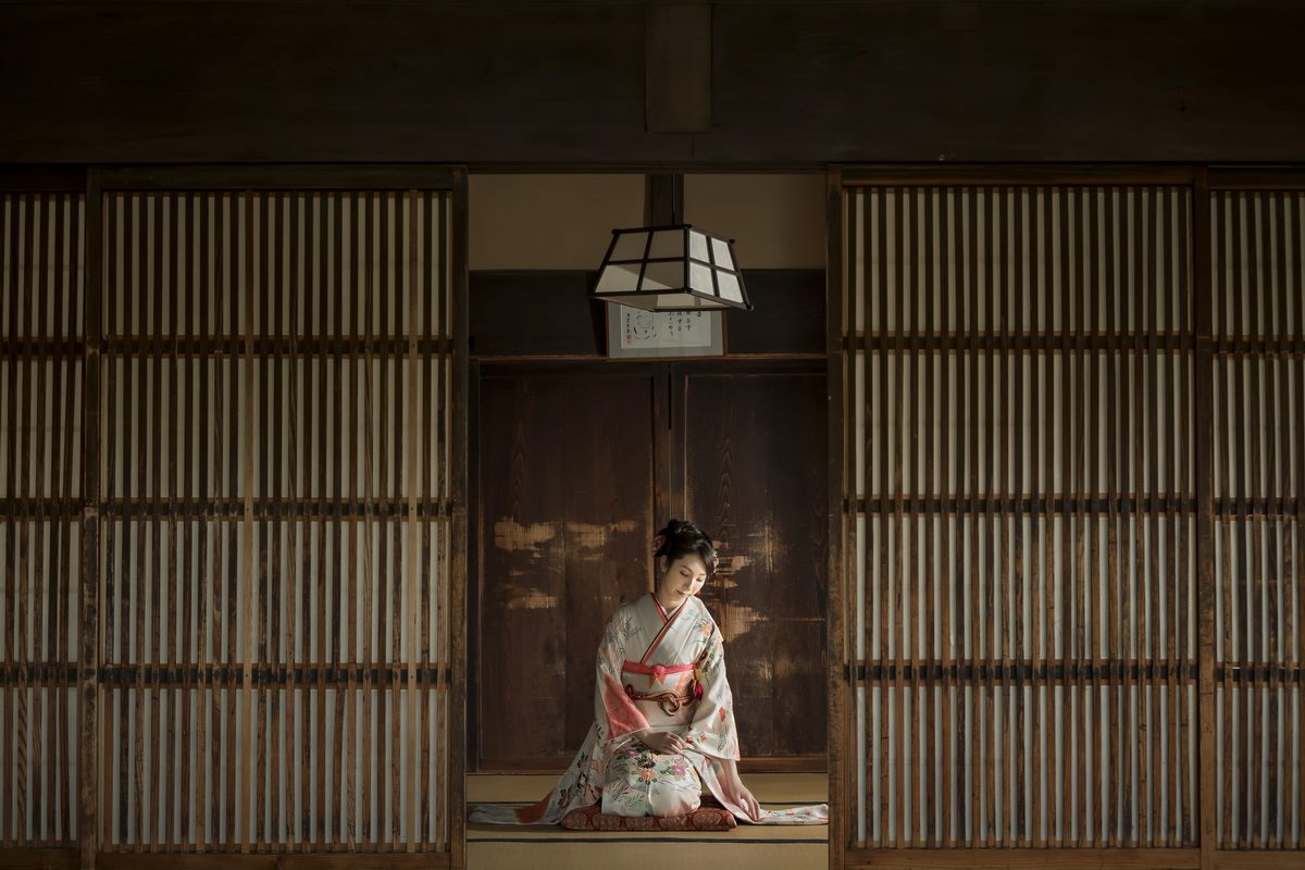 古民家の格子戸に囲まれた和室で、淡い色の振袖姿の女性が畳に正座する成人式前撮り。