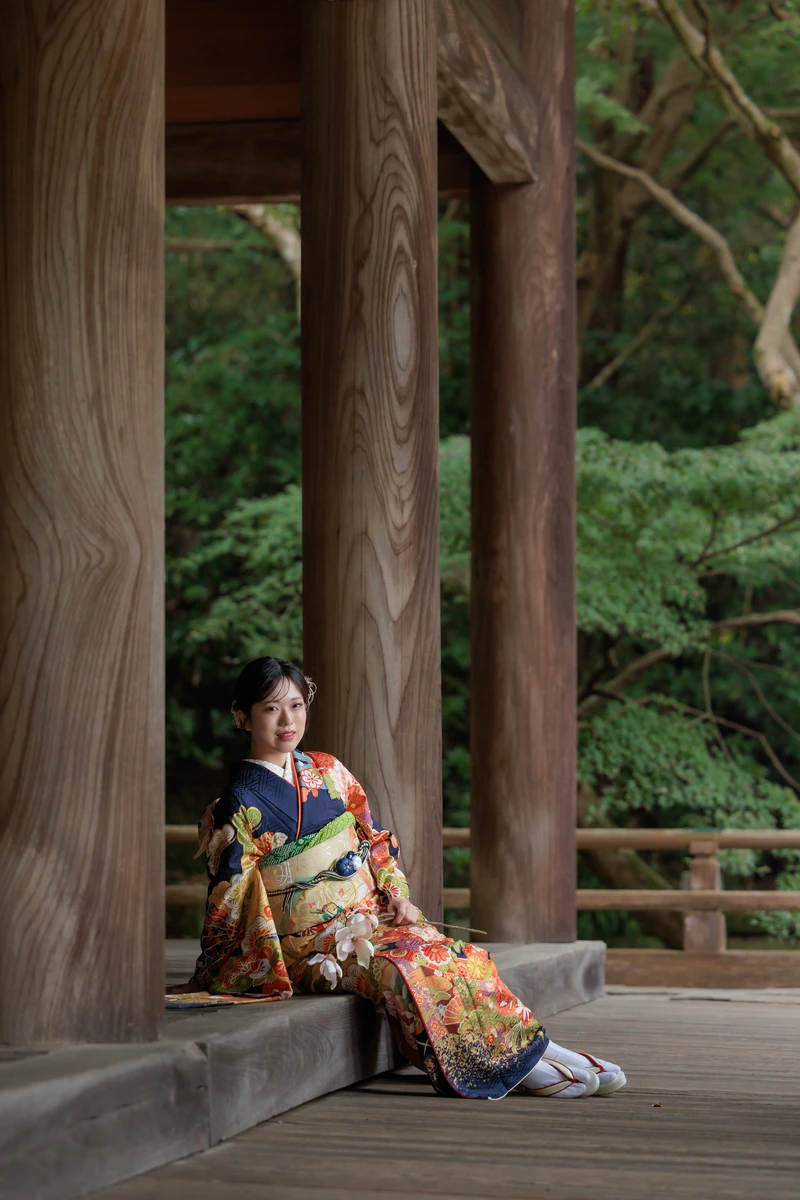 鎌倉妙本寺の回廊で、紺地に華やかな花柄の振袖姿の女性が木製の柱にもたれて座る成人式前撮り。