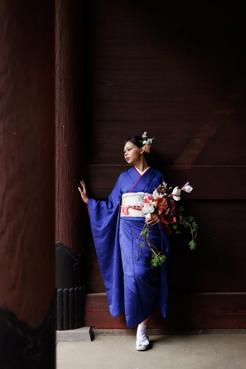鎌倉の寺院の木造建築を背景に、深い青の振袖姿の女性が洋風ブーケを持って立つ成人式前撮り。
