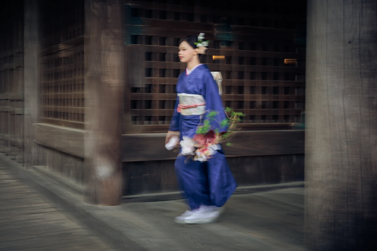 鎌倉の寺院回廊で、青い振袖姿の女性がブーケを手に歩く姿を、背景の流れを生かして捉えた成人式前撮り。
