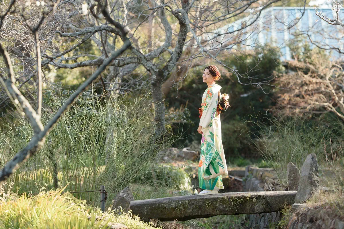 鎌倉の庭園で、白地に緑や橙色の植物文様が入った振袖姿の女性が石橋の上に立つ成人式前撮り。