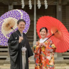 鎌倉・鎌倉本店の隣の神社で撮影した和装前撮り 鎌倉・鎌倉本店の隣の神社で色打掛を着用した新婦と紋付袴を着用した新郎が番傘を持って笑顔で写る和装前撮り
