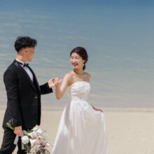 沖縄本島で夏に撮影した洋装前撮り 沖縄本島でウェディングドレスを着用した新婦とタキシードを着用した新郎が手を取って海沿いを歩く洋装前撮り