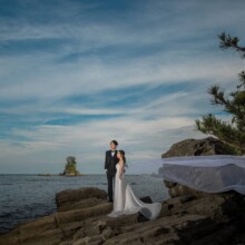 富山で夏に撮影した洋装前撮り 富山でウェディングドレスを着用した新婦とタキシードを着用した新郎がベールをなびかせて写る洋装フォトウェディング