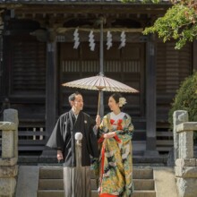 鎌倉・鎌倉本店の隣の神社で冬に撮影した和装前撮り 鎌倉・鎌倉本店の隣の神社で色打掛を着用した新婦と紋付袴を着用した新郎が番傘を持って歩いている和装ウェディングフォト