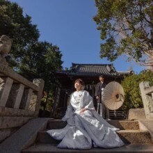 神社の石段に座る白無垢の新婦と和傘を持つ新郎の結婚式前撮り
