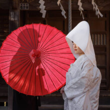 神社で赤い和傘を使った白無垢姿の新婦と新郎の結婚式前撮り