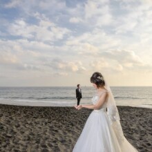 七里ヶ浜の砂浜で遠くに立つ新郎を見つめる花嫁。遊び心のある構図で撮影した洋装前撮りの一枚。