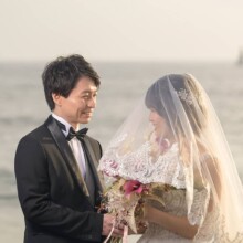 七里ヶ浜の海を背景に見つめ合う新郎新婦。柔らかなベール越しの表情が印象的な洋装フォトウェディング。