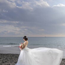 七里ヶ浜の海辺で風になびくドレスをまとい後ろ姿を見せる花嫁。夕景が美しい洋装前撮りのポートレート。