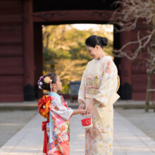 妙本寺の山門前で手をつなぎ見つめ合う母娘。華やかな着物姿で七五三のお祝いを楽しむ温かなワンシーン。