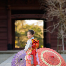 妙本寺の山門前で赤と紫の和傘を添え、振り返って微笑む晴れ着姿の女の子。七五三らしい華やかな記念カット。