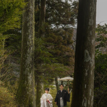 森の石畳を歩く和装の新郎新婦 男性が和傘を持っている