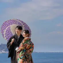 鎌倉・稲村ガ崎で冬に撮影した和装前撮り 鎌倉・稲村ガ崎で色打掛を着用した新婦と紋付き袴を着用した新郎が番傘を持って遠くを見つめている和装ウェディングフォト