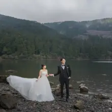 湖畔で手を取り合って並ぶ洋装の新郎新婦