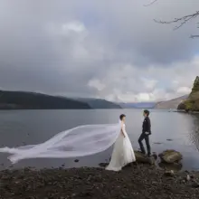 湖畔で向き合う洋装の新郎新婦 女性のベールが風になびいている