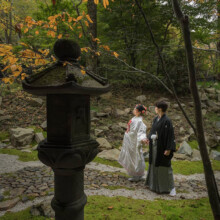 石灯籠越しに森の中の石畳を歩く和装の新郎新婦