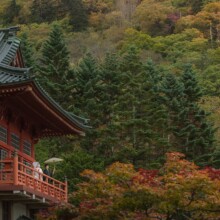 紅葉の森の中にある、朱塗りの神社の舞台に並ぶ和装の新郎新婦