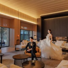 ホテルのロビーで並ぶ洋装の新郎新婦 男性は椅子に座り、女性はドレスの裾を持ち立っている