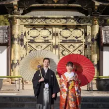 鎌倉・建長寺 2024.12.26 建長寺の唐門を背景に、白い和傘と赤い和傘を手に並んで立つ色打掛姿の新婦と紋付袴姿の新郎。格式ある建築を活かして撮影した色打掛前撮り・鎌倉和装前撮りのロケーションフォトです。