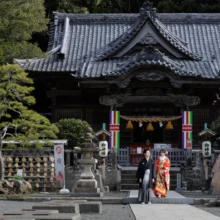 伊豆 和装 K様・Y様 伊豆の歴史ある神社の社殿前で、赤い色打掛の花嫁と黒紋付袴の新郎が並んで立つ、伝統的な和装ロケーション撮影