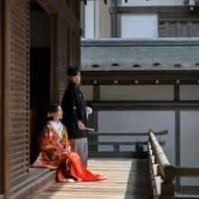 鎌倉 和装 K様・S様 2026.02.24 鎌倉建長寺回廊で、鮮やかな色打掛姿の花嫁が縁側に座り、黒紋付袴の新郎が後ろに立つ和装前撮りの横構図