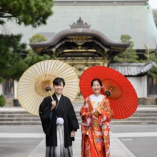 鎌倉 和装 K様・S様 2026.02.24 人気の建長寺の唐門を背景に、白い和傘を持つ黒紋付袴の新郎と赤い和傘を差す色打掛の花嫁が並ぶ鎌倉和装前撮り
