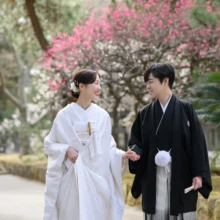 鎌倉 和装 K様・S様 2026.02.24 紅白の早春の花が咲く鎌倉の参道で、白無垢の花嫁と黒紋付袴の新郎が手を取り、見つめ合って歩く和装前撮り