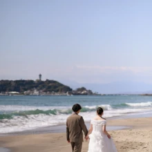 鎌倉・七里ガ浜で春に撮影した洋装前撮り 鎌倉・七里ガ浜でウェディングドレスを着用した新婦と持込のスーツを着用した新郎が江ノ島を背景に写る洋装前撮り
