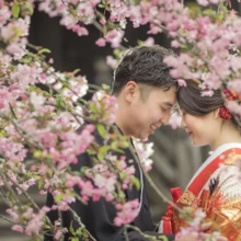 鎌倉 和装 K様・K様 2020.03.31 妙本寺の春の花に囲まれ、額を寄せ合う黒紋付袴の新郎と赤い色打掛の新婦を捉えた鎌倉和装前撮り