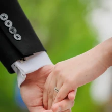 横浜 洋装 N様・K様 2022.04.17 新緑をぼかした背景の前で、新郎新婦が結婚指輪を着けた手を重ねて指を絡める横浜フォトウェディングの手元