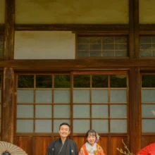 鎌倉 和装 N様・M様 2021.03.22 海蔵寺の本堂前で、黒紋付袴姿の新郎とオレンジの色打掛姿の新婦が赤い毛氈に正座し、両側に和傘を並べる