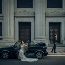 東京 洋装 N様・N様 2021.04.22 石造建築前の黒いオープンカーを挟み、ドレス姿の新婦とタキシード姿の新郎が立つ東京洋装前撮り