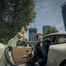 東京 洋装 N様・N様 2021.04.22 白いスポーツカーの開いたドア越しに手を伸ばすドレス姿の新婦と、車内から見上げるタキシード姿の新郎
