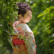 成人式撮影 H様 2021.05.09 檑亭の新緑に囲まれ、赤い髪飾りと振袖の帯結びを見せながら振り返って微笑む成人女性